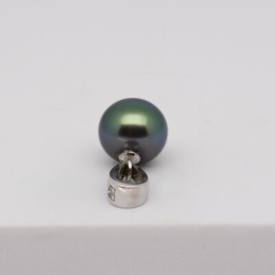 Sur fond blanc, le pendentif Aumoe présente une perle de Tahiti semi baroque d’un vert soutenu aux reflets bleus.
La perle, au lustre excellent, est suspendue à une bélière articulée en argent 925 rhodié, finement ornée d’éclats d’oxyde de zirconium.
L’éclairage neutre révèle la brillance du métal et la richesse chromatique de la perle, symbole du lien entre Manihi et Marseille.