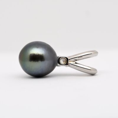 Sur fond blanc, le pendentif Moke présente une perle de Tahiti semi baroque ovale de 10 mm à la couleur bleu roi-vert naturelle et au lustre excellent. La perle est suspendue à une bélière massive en argent 925 rhodié, ornée d’un éclat d’oxyde de zirconium. La photo met en valeur la profondeur des teintes marines de la perle et la brillance du métal, dans une lumière neutre.