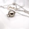 Photo sur fond blanc d’un collier nommé Eva, composé d’une fine chaîne en argent 925 rhodié de 48 cm. Au centre, une véritable perle de Tahiti semi-baroque de couleur verte naturelle est suspendue, avec un diamètre d’environ 9,7 mm. La perle présente un lustre brillant et des reflets profonds. L’ensemble dégage une impression de sobriété, d’élégance et de bijou artisanal conçu pour être porté au quotidien.