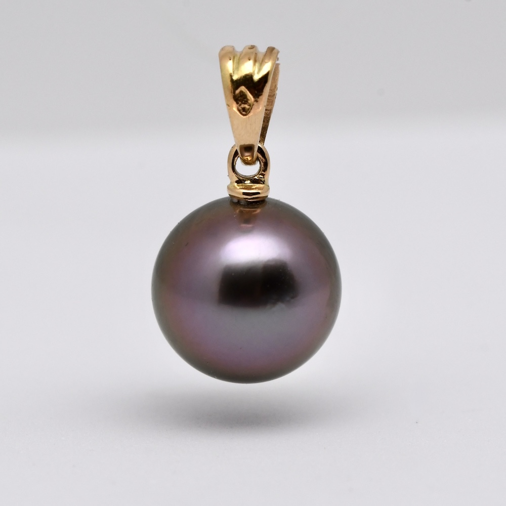 Le pendentif perle Kaloke (Rose en Hawaien) est en or jaune 18 k qui met en lumière une superbe perle de Tahiti ronde de 10,1 mm, sélectionnée pour sa qualité et surtout pour sa couleur violine exceptionnelle, subtilement enrichie de nuances de vert profond. Cette combinaison de teintes naturelles offre un rendu visuel fascinant, oscillant entre reflets pourpres et éclats végétaux, selon l’intensité de la lumière.