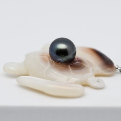 Honu – Pendentif tortue en nacre et perle de Tahiti Honu est une pièce artisanale unique qui réunit deux trésors issus de l'huître perlière : la blancheur lumineuse de la nacre et les nuances profondes d'une véritable perle de culture de Tahiti .